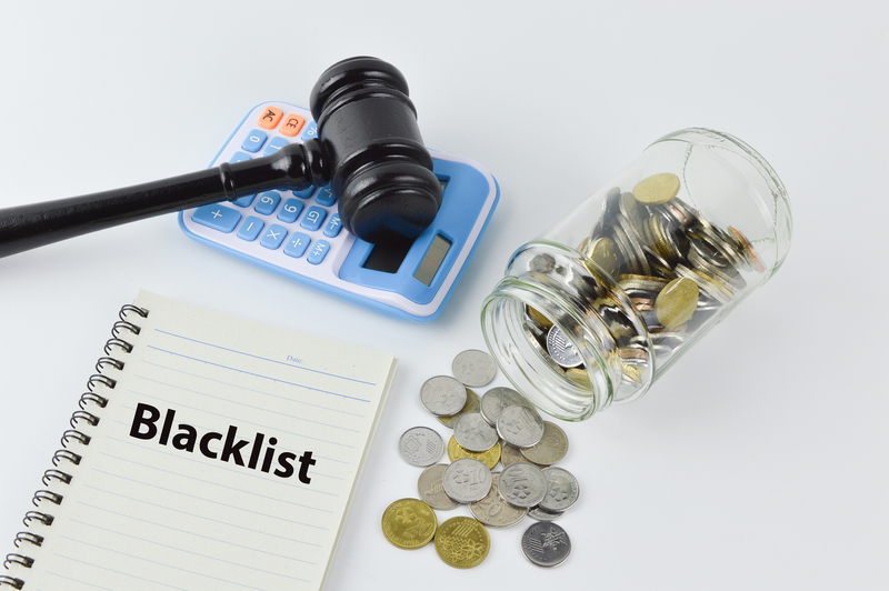 Penning down blacklisted money lenders in Singapore in a notebook and a picture of judge gravel, calculator and coins.