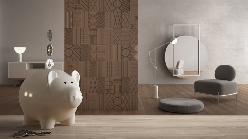 White piggy bank with coins sitting on wooden tabletop, and modern furniture. All made possible with a furniture loan in Singapore.