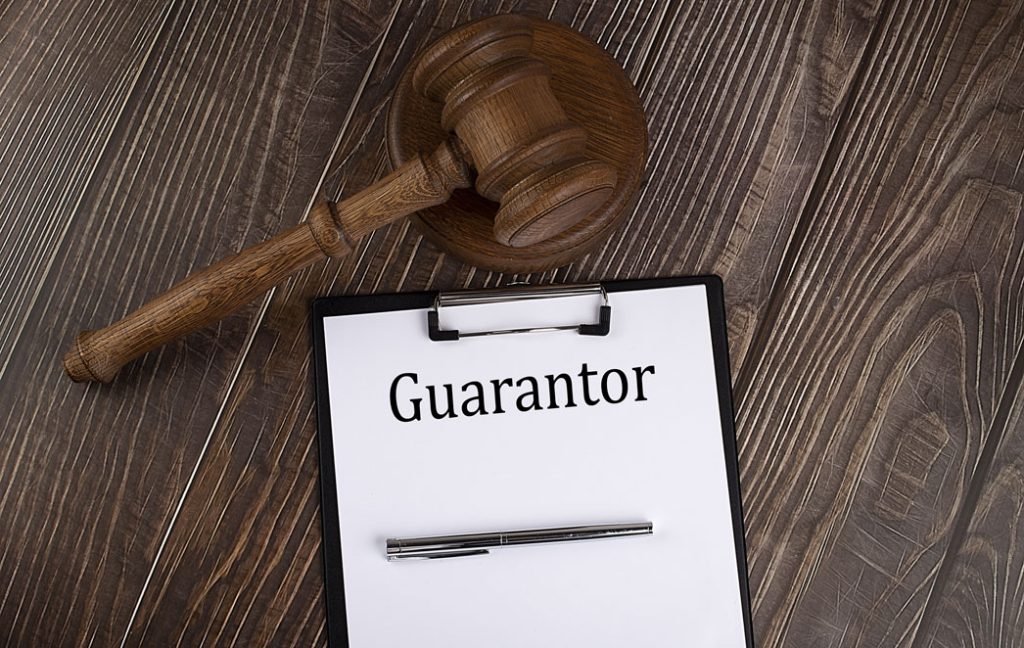 The word ‘Guarantor’ written on paper with clipboard next to a gavel on a wooden table, representing loan guarantor requirements in Singapore